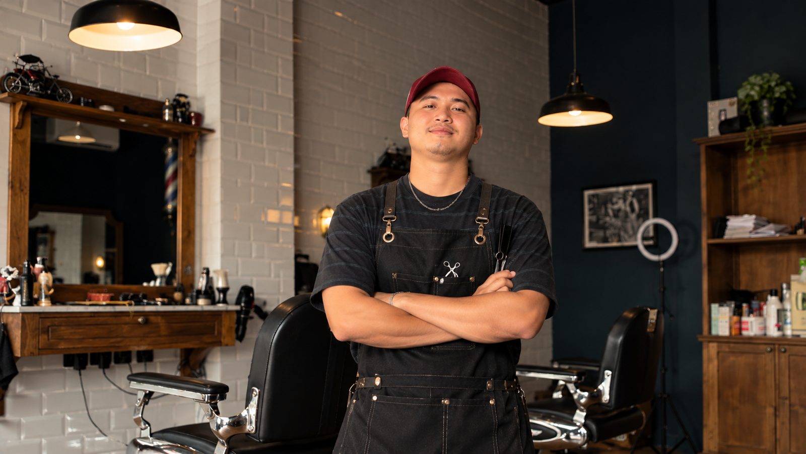 Fauzan Damansyara (Zan) in his barber apron, arms crossed, in a barbershop